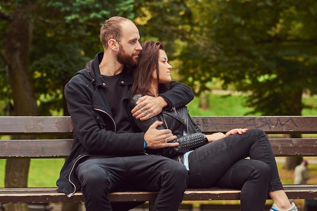 Atractiva pareja moderna abrazándose en un banco en el parque. Disfrutando de su amor y la naturaleza.