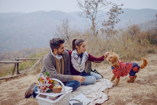 Atractiva pareja multicultural sentado en una manta y jugando con su perro. Picnic en el concepto de otoño.