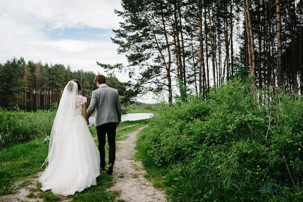 Atractiva pareja de recién casados está caminando de regreso por un sendero en un bosque verde Momento feliz y alegre