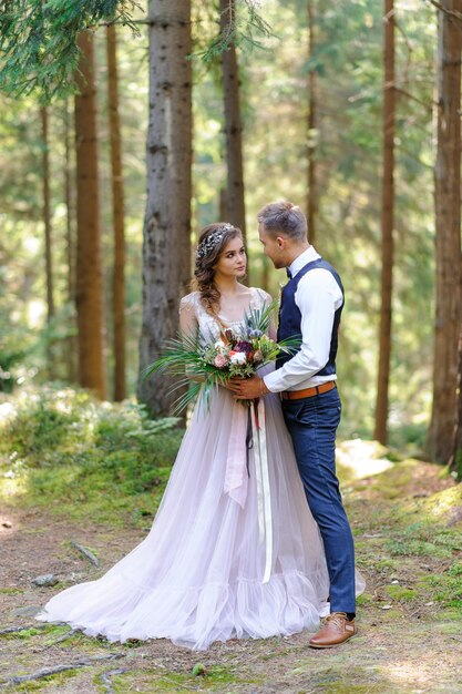 Una atractiva pareja de recién casados, un momento feliz y alegre. Un hombre y una mujer se afeitan y se besan con ropa de fiesta. Boda de estilo bohemio en el bosque al aire libre.