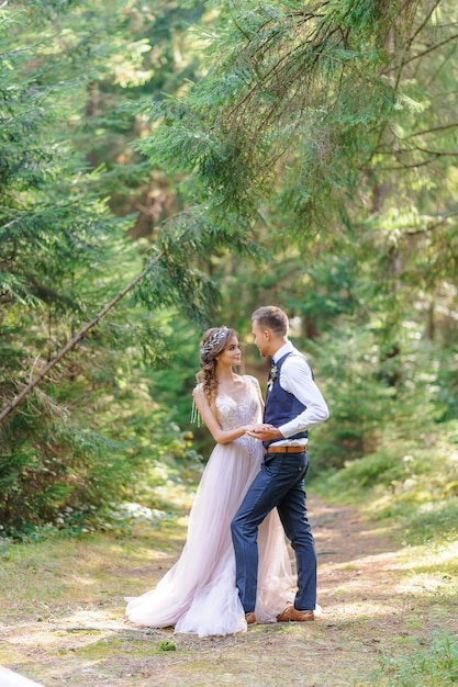 Una atractiva pareja de recién casados, un momento feliz y alegre. Un hombre y una mujer se afeitan y se besan con ropa de fiesta. Boda de estilo bohemio en el bosque al aire libre.