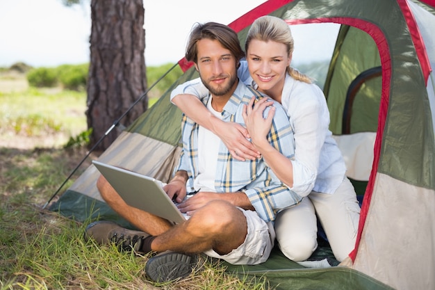 Atractiva pareja sentada junto a su tienda utilizando la computadora portátil sonriendo a la cámara