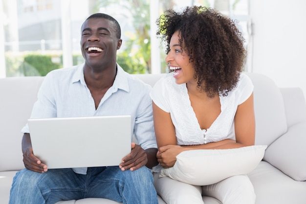 Atractiva pareja usando laptop juntos en el sofá en casa en la sala de estar