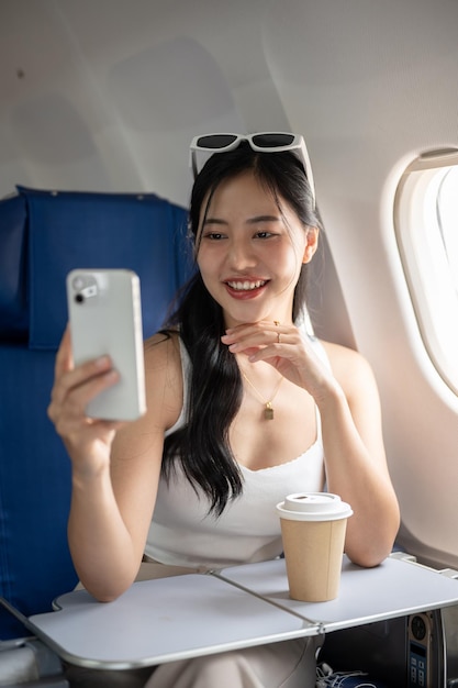 Una atractiva pasajera asiática se toma una selfie con su teléfono inteligente durante el vuelo