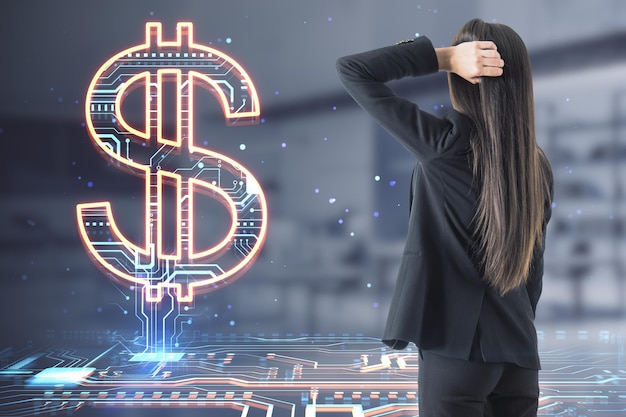 Foto atractiva y pensativa joven empresaria europea mirando el holograma de signo de dólar que brilla intensamente creativo en el fondo interior de la oficina borrosa tecnología bancaria en línea y concepto de moneda