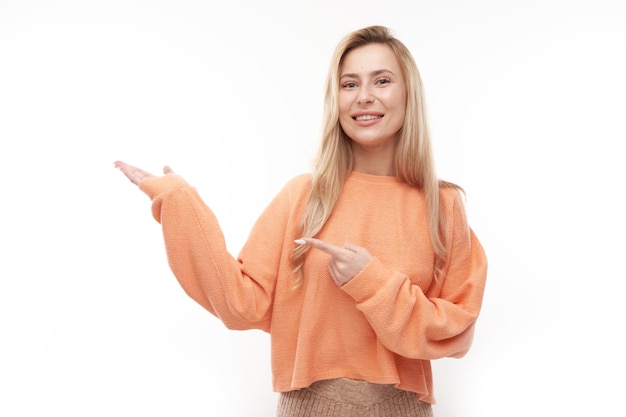 Una atractiva promotora rubia sosteniendo algo en la mano demostrando un espacio vacío con cara emocionada aislada de fondo blanco