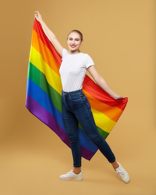 Atractiva rubia posando con una bandera LGBT arcoíris. sesión de fotos en el estudio sobre un fondo amarillo.