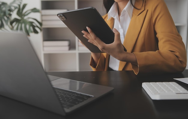 Atractiva y sonriente mujer de negocios asiática joven que trabaja en la oficina en casa Mujer asiática que trabaja en una computadora portátil con tableta