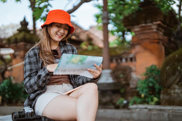 Foto una atractiva turista asiática mirando un mapa de un destino turístico durante un descanso sentada