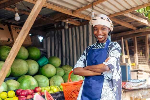 Foto atractiva vendedora africana en un puesto de frutas con los brazos cruzados