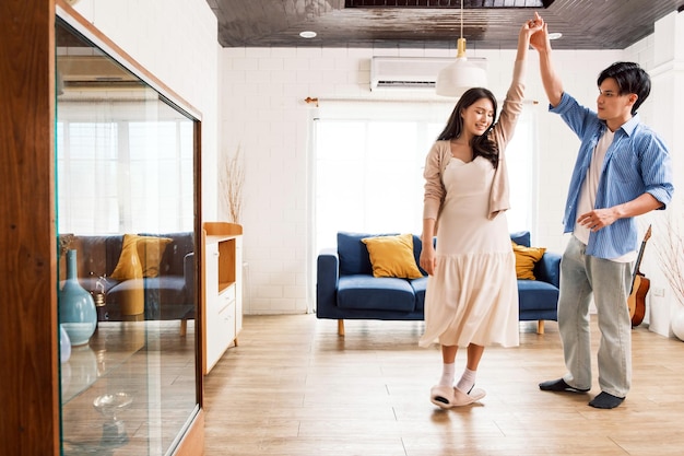 Atractivas parejas jóvenes asiáticas disfrutan de un encantador baile romántico en la sala de estar del apartamento. Una familia pasa tiempo de calidad junta después de mudarse a un nuevo hogar Imagen con espacio para copiar