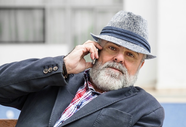 Atractivo anciano con barba y sombrero hablando por teléfono