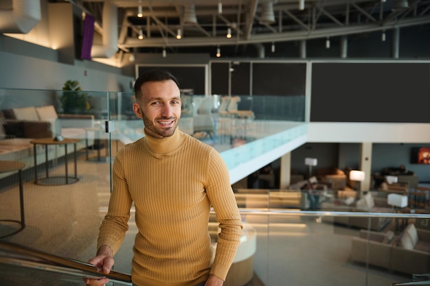 Atractivo y apuesto hombre de mediana edad con ropa informal sube las escaleras en el salón de la terminal de salidas del aeropuerto internacional mientras espera un vuelo. Empresario en un viaje de negocios