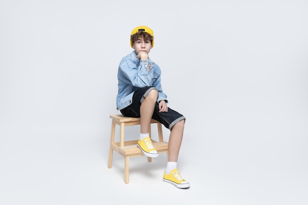 Atractivo chico adolescente con estilo sentado en una silla