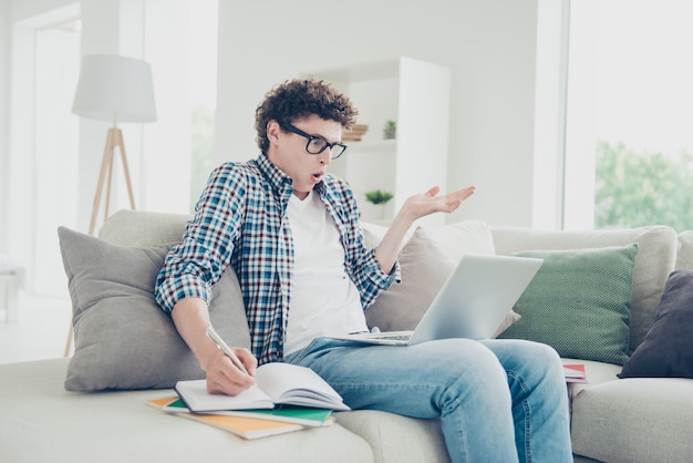 Atractivo chico confundido estudiante nerd en casa haciendo los deberes universitarios