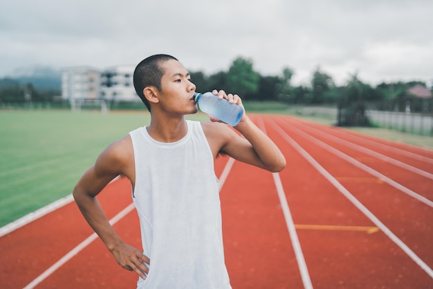 Atractivo corredor de hombre deportivo asiático cansado y sediento después de correr entrenamiento bebiendo agua Concepto de hombre deportivo