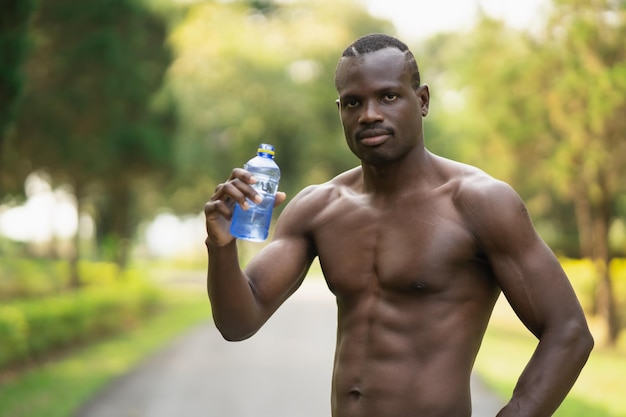 Atractivo deportista africano cansado y sediento después de hacer ejercicio bebiendo agua. Concepto de hombre deportivo