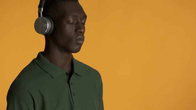 Atractivo y elegante chico afroamericano con auriculares cerrando los ojos escuchando música aislada en un fondo colorido