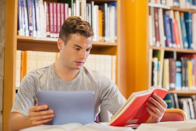 Atractivo estudiante sonriente con tableta y libro de explotación