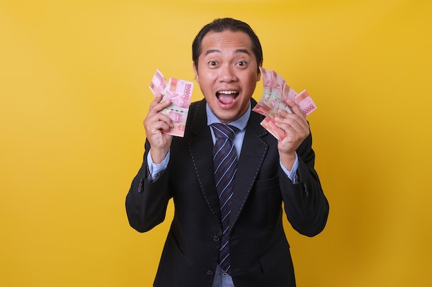 Atractivo hombre asiático con traje de negocios parado en un fondo amarillo que muestra dinero cien