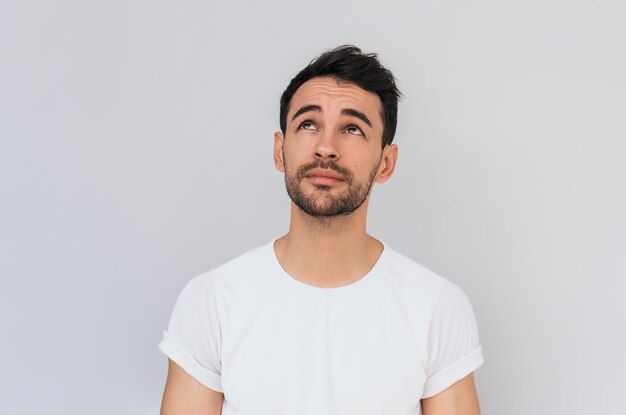 Foto atractivo hombre barbudo que viste camiseta blanca se ve cuidadosamente aislado sobre fondo blanco con espacio de copia para su anuncio o texto promocional concepto de estilo de vida y emociones de la gente