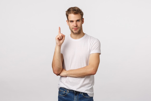 Atractivo hombre barbudo rubio con camiseta blanca levanta el dedo índice