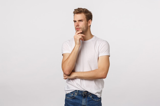 Atractivo hombre barbudo rubio en camiseta blanca pensando