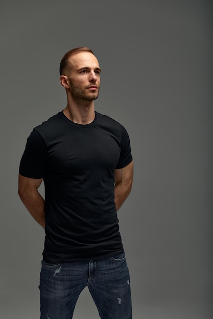 Un atractivo hombre blanco con jeans y camisas negras está en pleno crecimiento contra un fondo gris Copiar espacio
