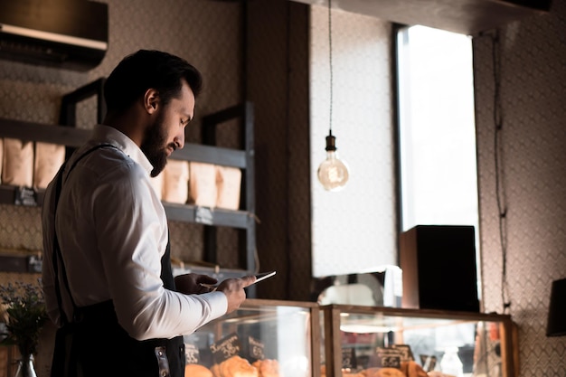 Atractivo hombre caucásico en delantal (propietario de una pequeña empresa o barista) que trabaja en una cafetería de panadería