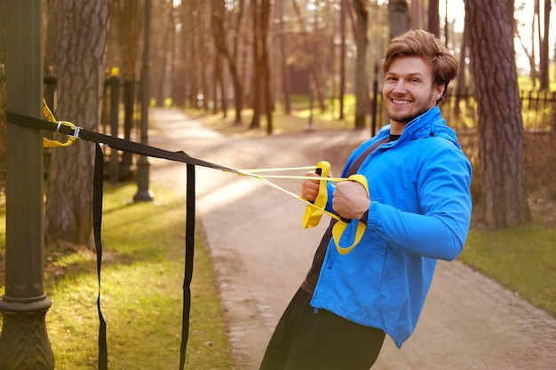 Atractivo hombre deportivo haciendo ejercicio con tiras de fitness trx en un parque.