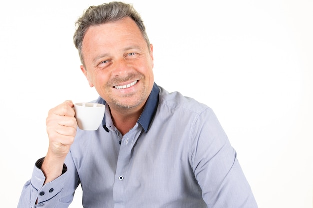 Foto atractivo hombre guapo sonriente con bebida caliente taza de café en mano sobre fondo blanco.