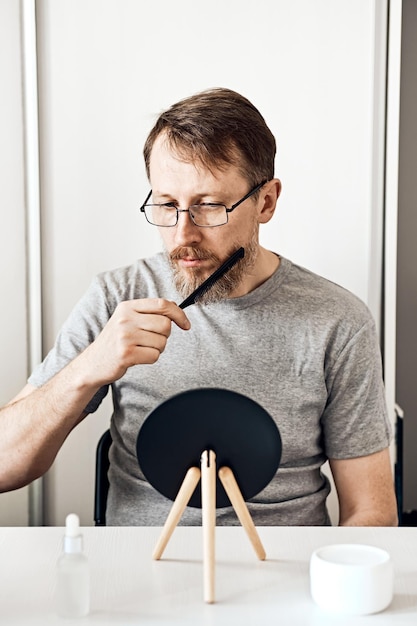 Un atractivo hombre de mediana edad endereza su barba frente a un espejo Aspecto natural cabello rubio claro y pecas barba con canas Enfoque suave