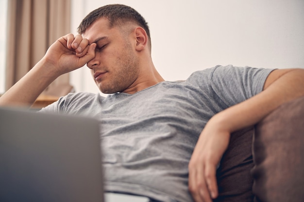 Atractivo hombre morena con los ojos cerrados después de pasar tiempo con el portátil