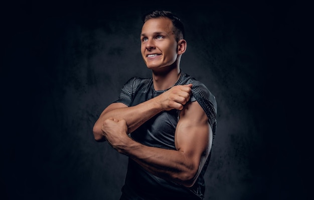 Un atractivo hombre musculoso vestido con ropa deportiva muestra sus músculos en un fondo gris.