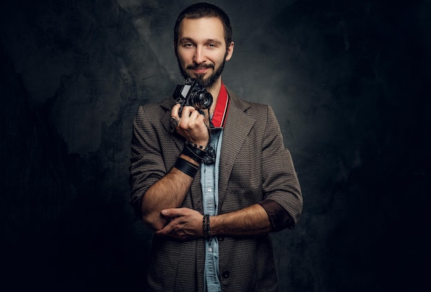 Atractivo hombre pensativo con cámara fotográfica está posando para el fotógrafo en un estudio fotográfico oscuro.
