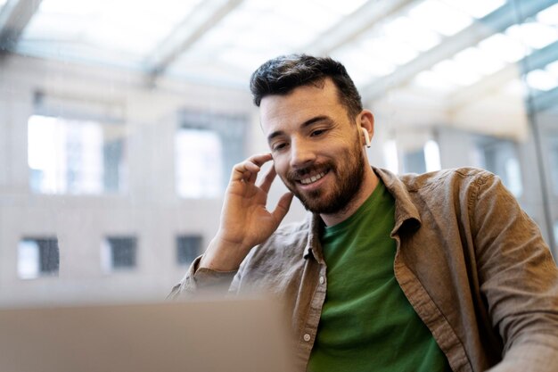 Atractivo hombre sonriente en auriculares inalámbricos con videoconferencia usando una computadora portátil