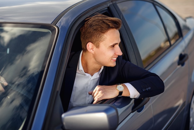 Atractivo hombre sonriente guapo en un traje de negocios conduciendo un automóvil caro