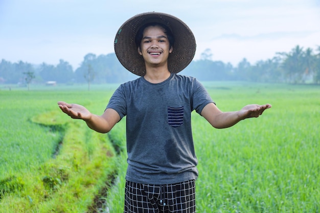 Atractivo joven agricultor asiático alegre de pie sonriendo y extendiendo los brazos mostrando el éxito a growi