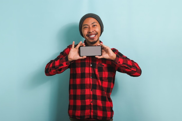 Atractivo joven asiático muestra teléfono móvil con espacio de copia aislado en fondo azul