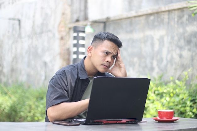 Atractivo joven asiático usando una laptop confundido en el espacio de coworking con cara infeliz