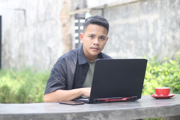 Atractivo joven asiático usando laptop en espacio de coworking con cara feliz