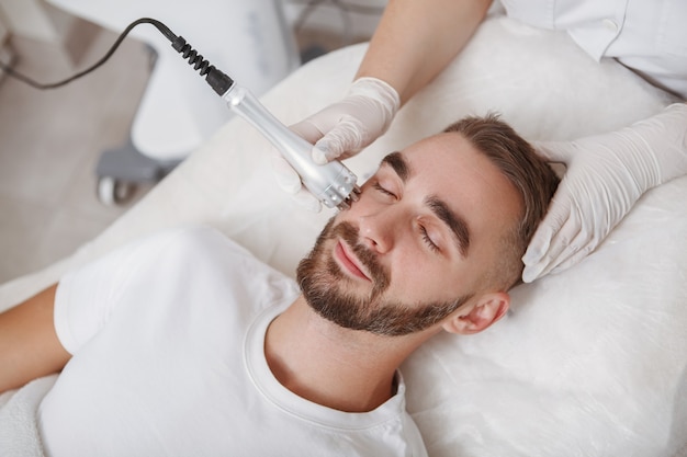 Atractivo joven barbudo disfrutando de tratamiento facial de cosmetología de hardware