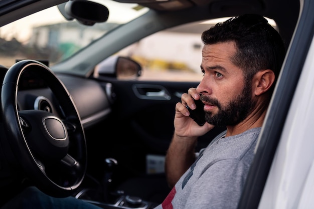 Atractivo joven barbudo hablando por teléfono móvil mientras descansa sentado dentro de su auto ocio y tecnología del concepto de comunicación