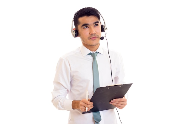 Atractivo joven con cabello oscuro en camisa con corbata azul usando auriculares y sosteniendo una carpeta