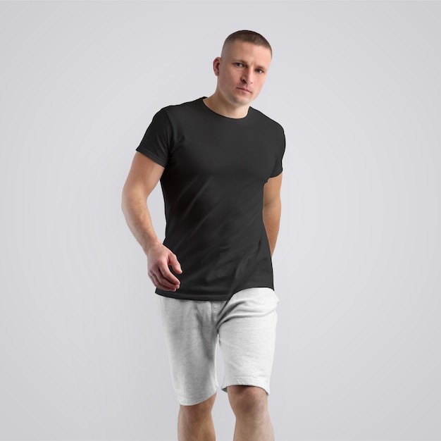 Atractivo joven caucásico con una camiseta negra y pantalones cortos grises tejidos sobre un fondo blanco de estudio. Postura frontal. La plantilla se puede utilizar en su diseño.