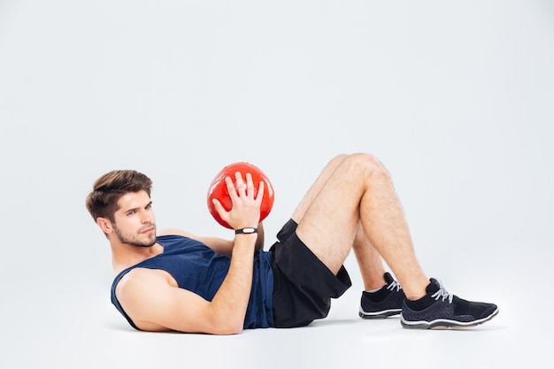 Foto atractivo joven deportista sosteniendo pelota redd y haciendo abdominales