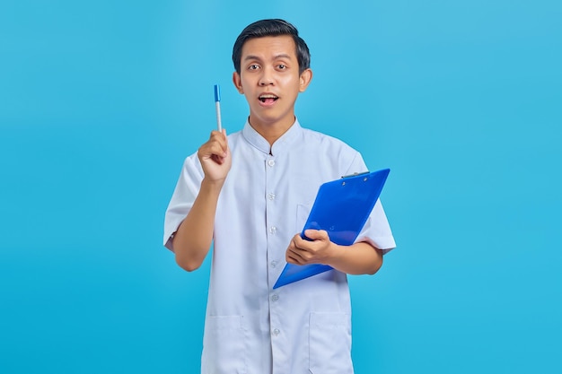 Atractivo joven enfermero asiático sosteniendo la pluma y tener una buena idea aislada sobre fondo azul.