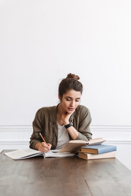 Foto atractivo joven estudiante haciendo los deberes en el interior, leyendo libros