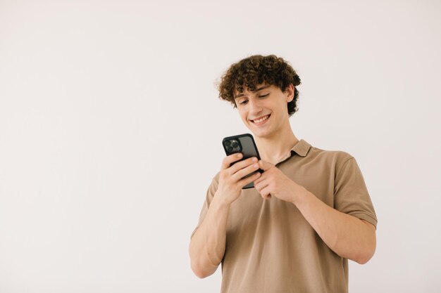 Atractivo joven estudiante masculino usando el teléfono en un fondo blanco con espacio libre