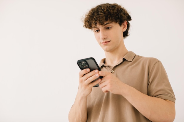 Atractivo joven estudiante masculino usando el teléfono en un fondo blanco con espacio libre